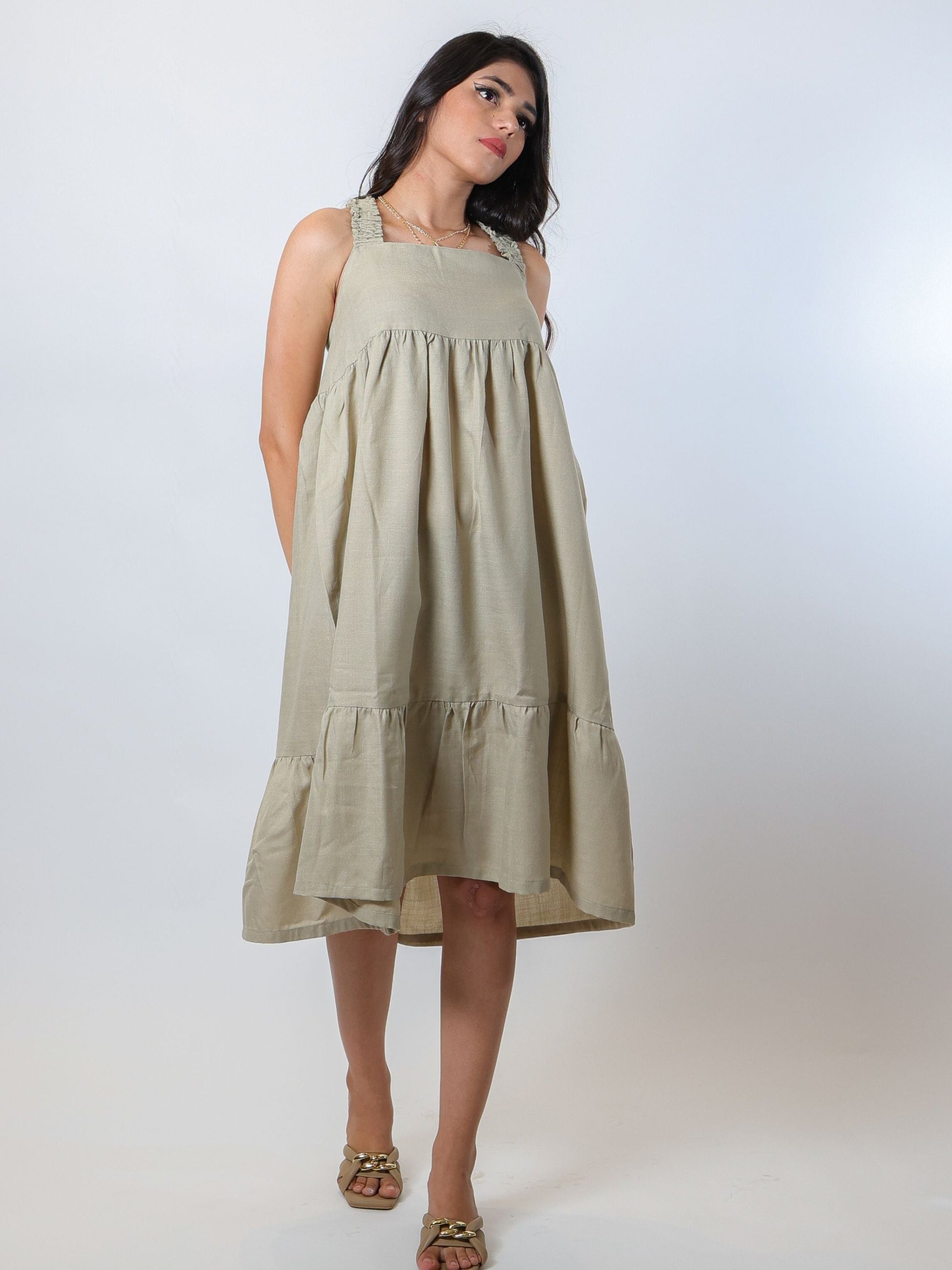 Flattering green knee-length tiered dress made from a soft linen blend fabric, featuring criss-cross smocked back and smocked straps, lightweight and airy for summer and spring, perfect for pairing with open-toed sandals and bling accessories.