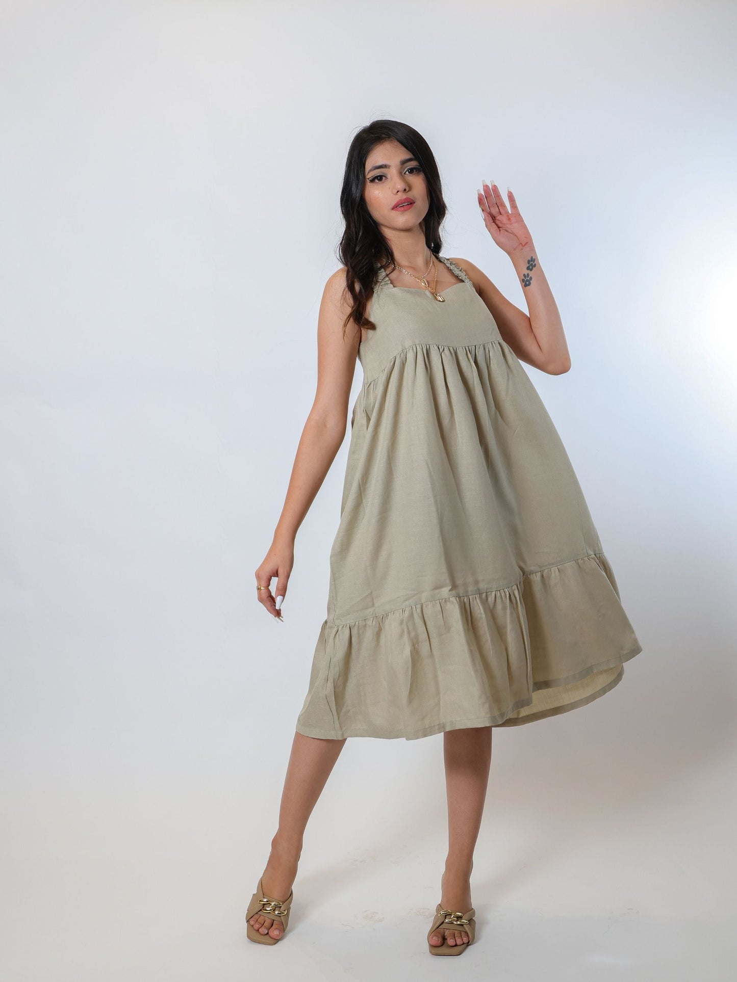 Flattering green knee-length tiered dress made from a soft linen blend fabric, featuring criss-cross smocked back and smocked straps, lightweight and airy for summer and spring, perfect for pairing with open-toed sandals and bling accessories.