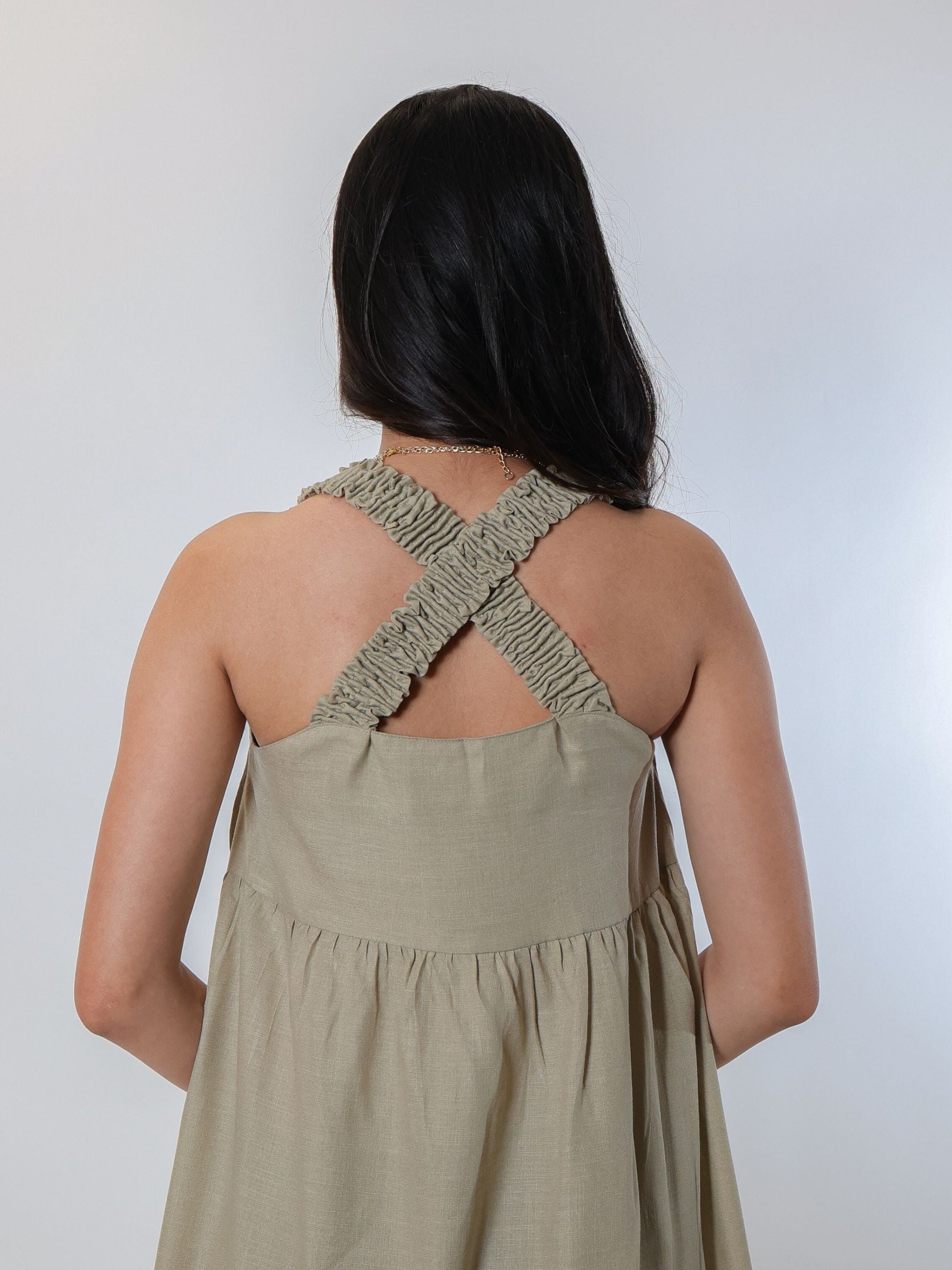 Flattering green knee-length tiered dress made from a soft linen blend fabric, featuring criss-cross smocked back and smocked straps, lightweight and airy for summer and spring, perfect for pairing with open-toed sandals and bling accessories.